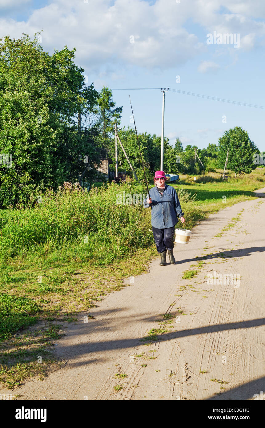 Rural lifestyle 2013. The woman goes fishing. Village sand road, sunny day. Stock Photo