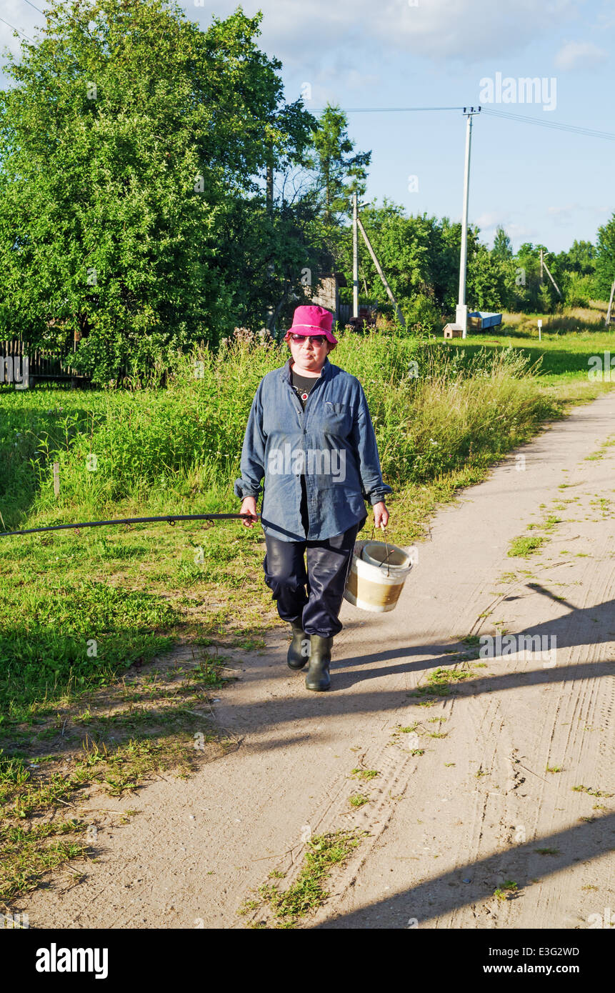 Rural lifestyle 2013. The woman goes fishing. Village sand road, sunny day. Stock Photo