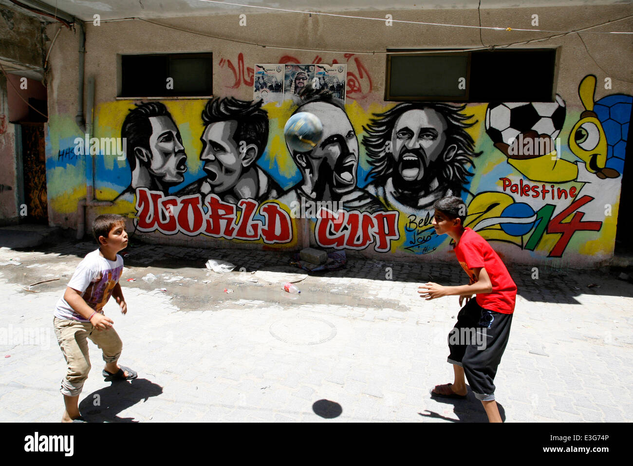 KHAN YUNIS, GAZA STRIP, PALESTINE - JUNE 23: A Palestinian boys play a ball in front of graffiti wall murals depicting football players the participants at 2014 World Cup Brazil (LtoR) Portugal's Cristiano Ronaldo, Argentina's Lionel Messi, Netherlands' Arjen Robben and Italy's Andrea Pirlo, in the Khan Yunis refugee camp in the southern Gaza Strip on June 23, 2014. (Photo by Abed Rahim Khatib /Pacific Press) Stock Photo