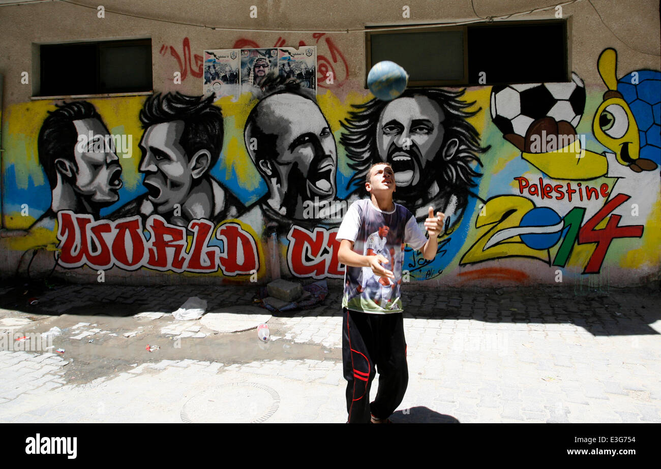 KHAN YUNIS, GAZA STRIP, PALESTINE - JUNE 23: A Palestinian boy plays a ball in front of graffiti wall murals depicting football players the participants at 2014 World Cup Brazil (LtoR) Portugal's Cristiano Ronaldo, Argentina's Lionel Messi, Netherlands' Arjen Robben and Italy's Andrea Pirlo, in the Khan Yunis refugee camp in the southern Gaza Strip on June 23, 2014. (Photo by Abed Rahim Khatib /Pacific Press) Stock Photo