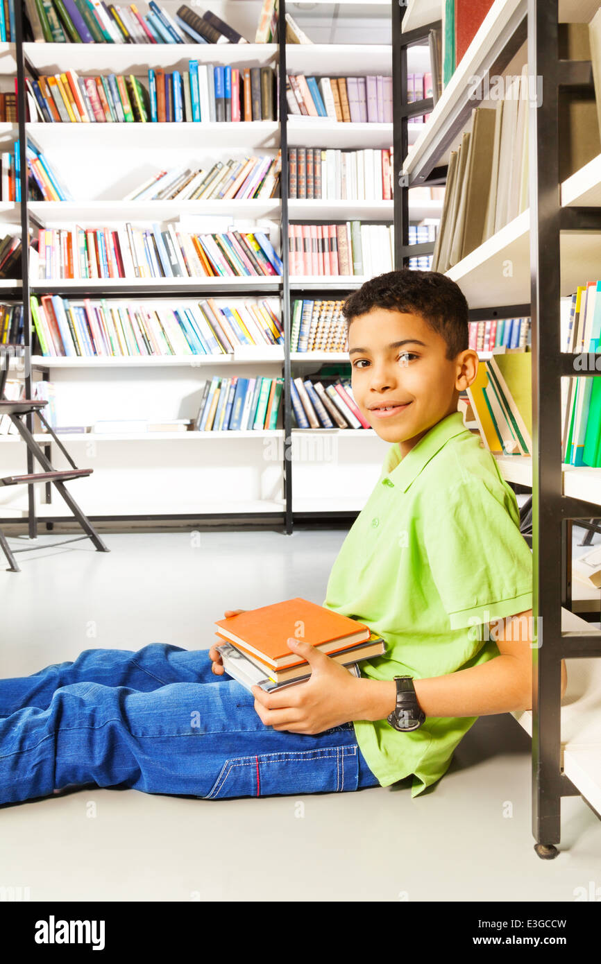 Smiling pupil with pile of books sitting on floor Stock Photo - Alamy
