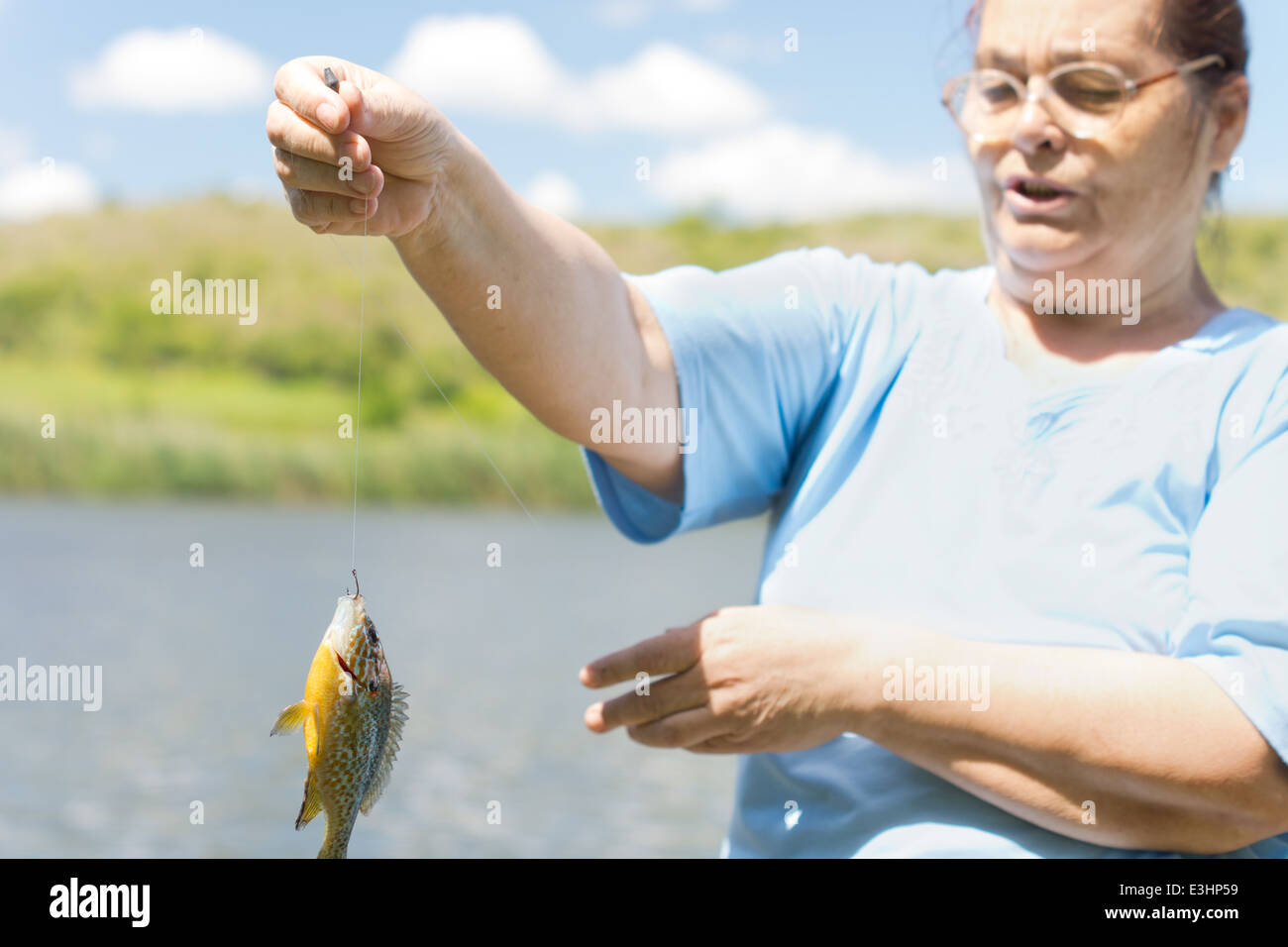 Middle aged woman holding up a fish dangling from the end of a fishing line  as she fishes on a freshwater lake Stock Photo - Alamy