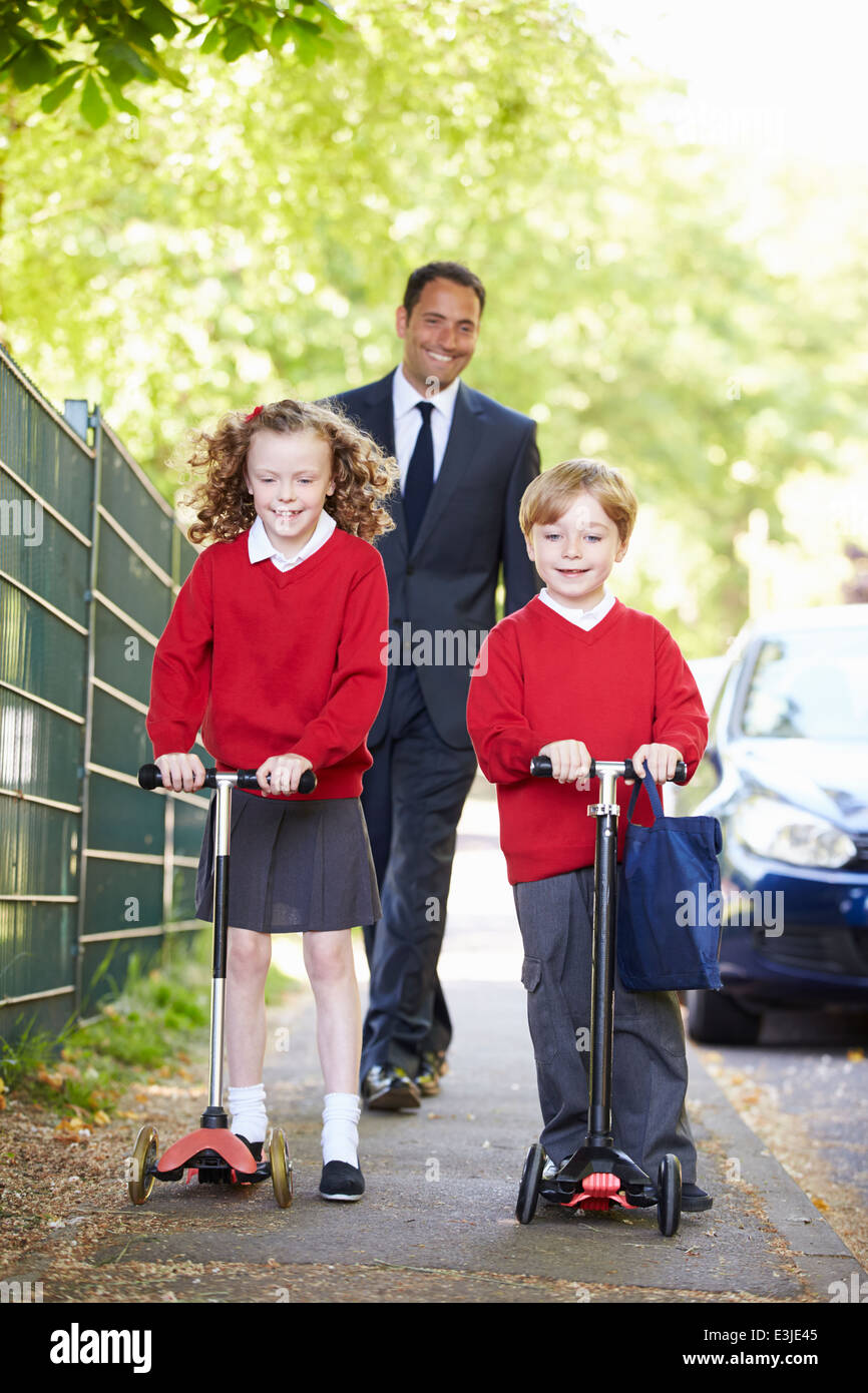 Children Riding Scooters On Their Way To School With Father Stock Photo