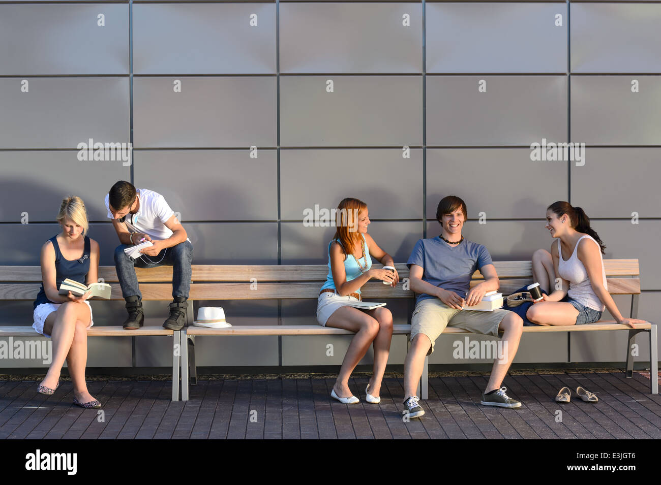 College students sitting on bench by modern wall outside campus Stock Photo