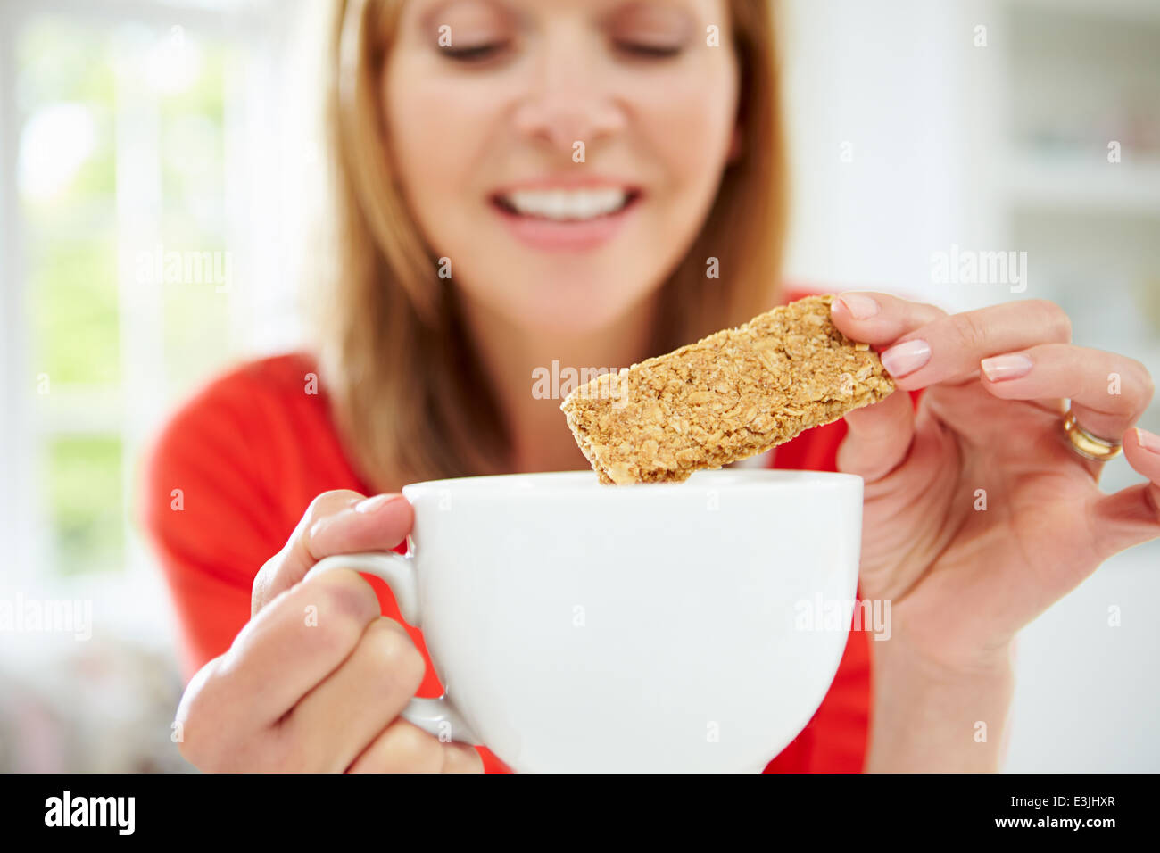 Woman Dipping Biscuit Into Hot Drink At Home Stock Photo
