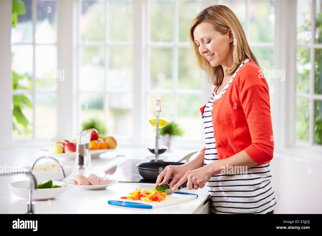 Woman Standing At Counter Preparing Meal In Kitchen Stock Photo
