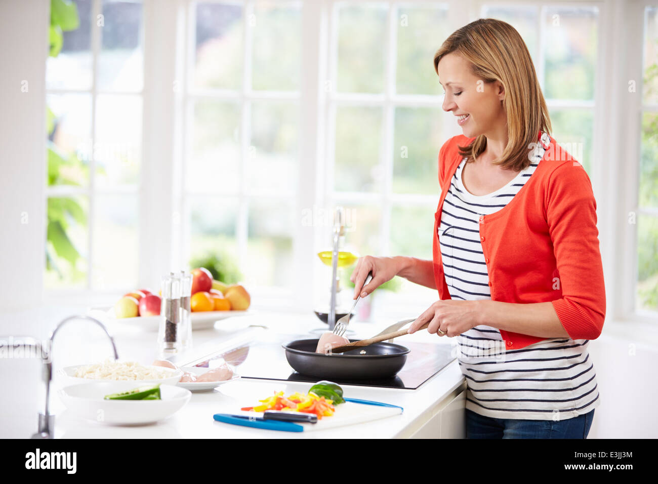 Woman Standing At Hob Preparing Meal In Kitchen Stock Photo