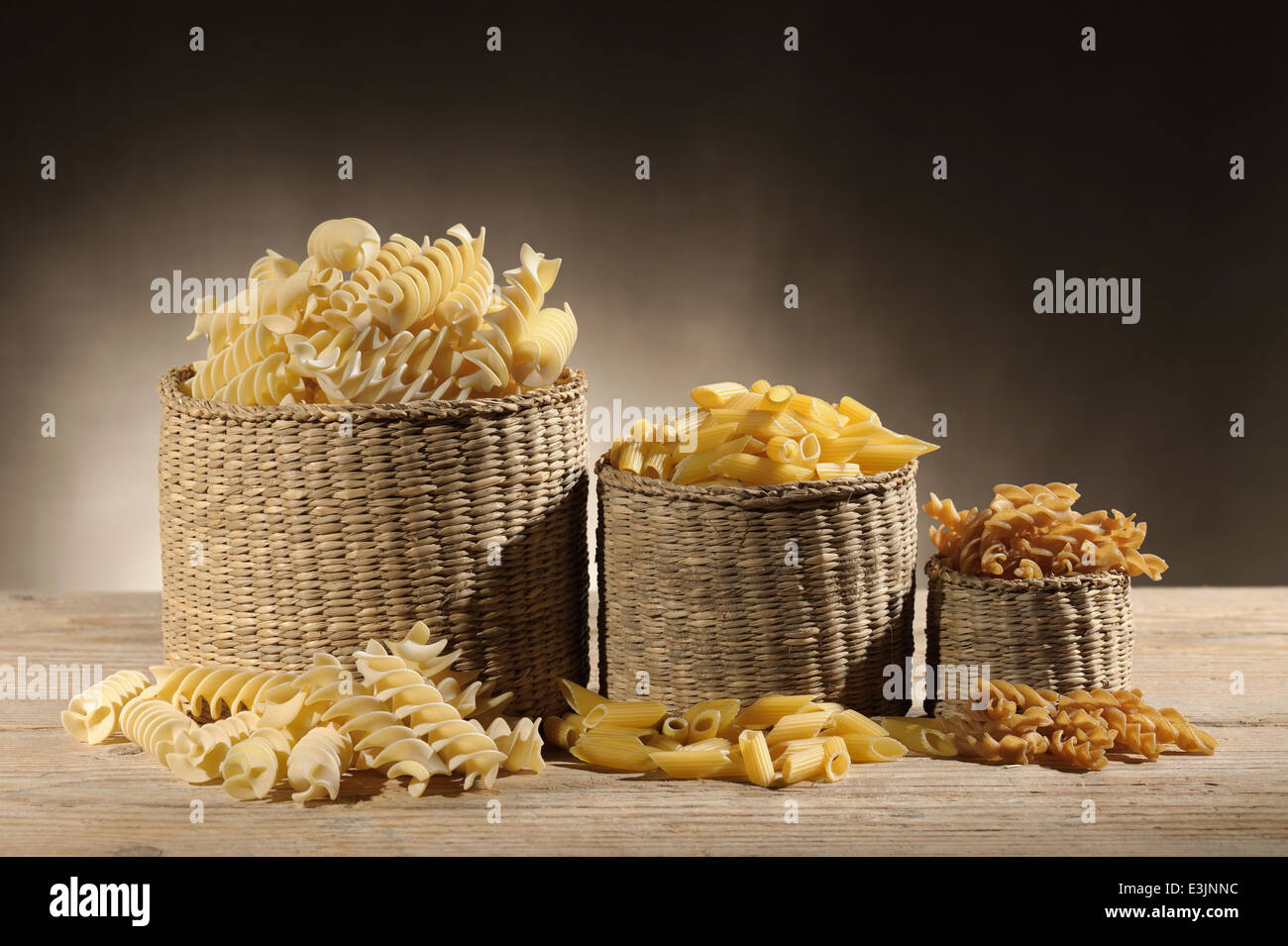 straw baskets with variety of uncooked pasta on wooden table Stock Photo