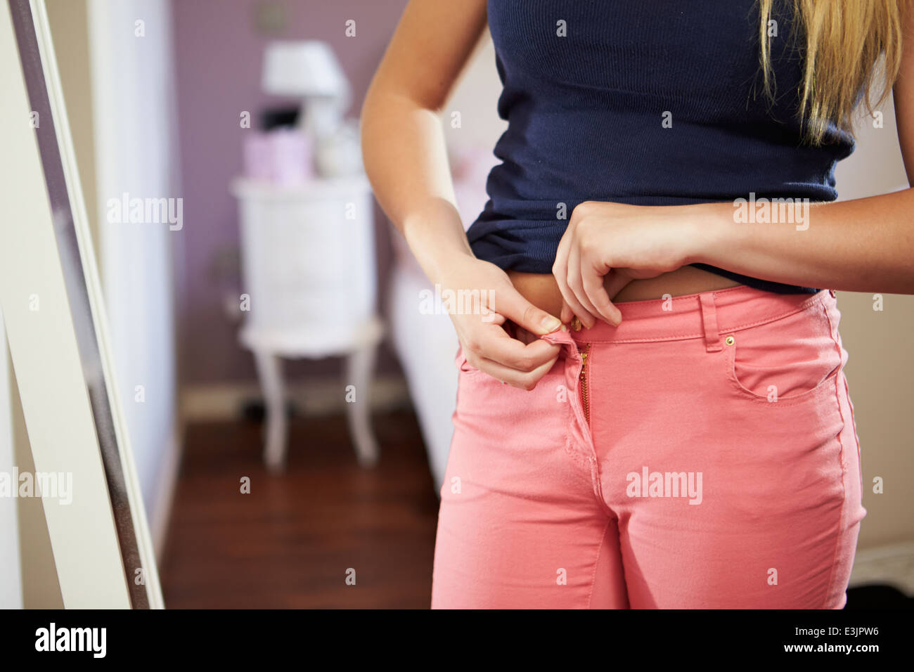 Close Up Of Teenage Girl Fastening Trousers In Bedroom Stock Photo