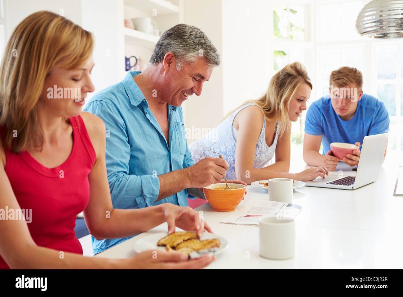Teenage Family Having Breakfast In Kitchen With Laptop Stock Photo