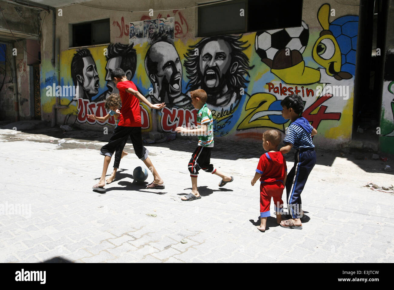 Gaza, Gaza Strip, Palestinian Territories. 23rd June, 2014. A Palestinian boys play a ball in front of graffiti wall murals depicting football players the participants at 2014 World Cup Brazil (LtoR) Portugal's Cristiano Ronaldo, Argentina's Lionel Messi, Netherlands' Arjen Robben and Italy's Andrea Pirlo, in the Khan Yunis refugee camp in the southern Gaza Strip. on June 23, 2014. © Abed Rahim Khatib/NurPhoto/ZUMAPRESS.com/Alamy Live News Stock Photo