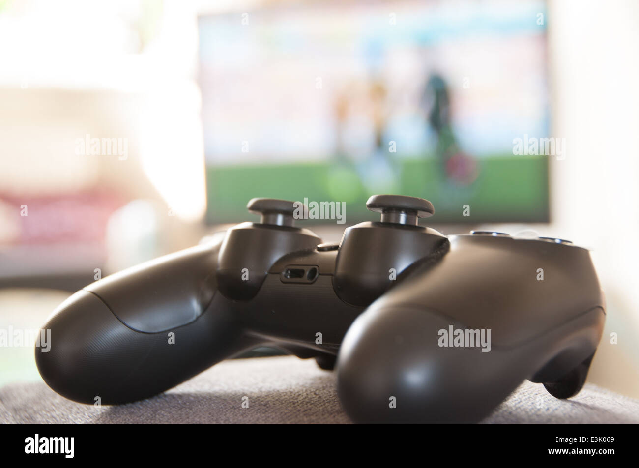 games controller sitting on a sofa arm with football game going on in the background Stock Photo