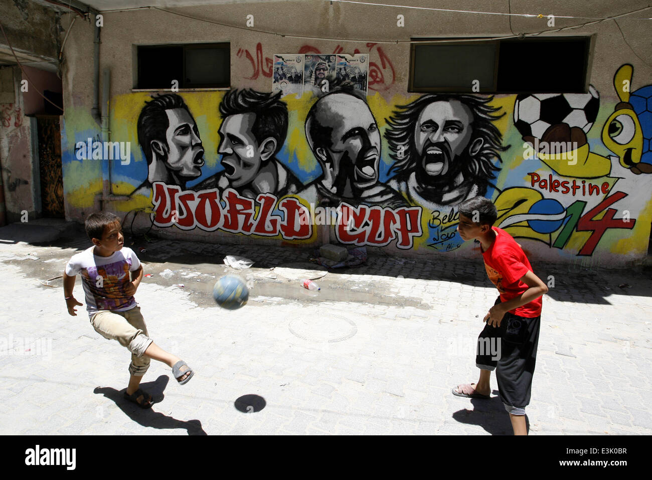 Gaza, Gaza Strip, Palestinian Territories. 23rd June, 2014. A Palestinian boys play a ball in front of graffiti wall murals depicting football players the participants at 2014 World Cup Brazil (LtoR) Portugal's Cristiano Ronaldo, Argentina's Lionel Messi, Netherlands' Arjen Robben and Italy's Andrea Pirlo, in the Khan Yunis refugee camp in the southern Gaza Strip. on June 23, 2014. © Abed Rahim Khatib/NurPhoto/ZUMAPRESS.com/Alamy Live News Stock Photo