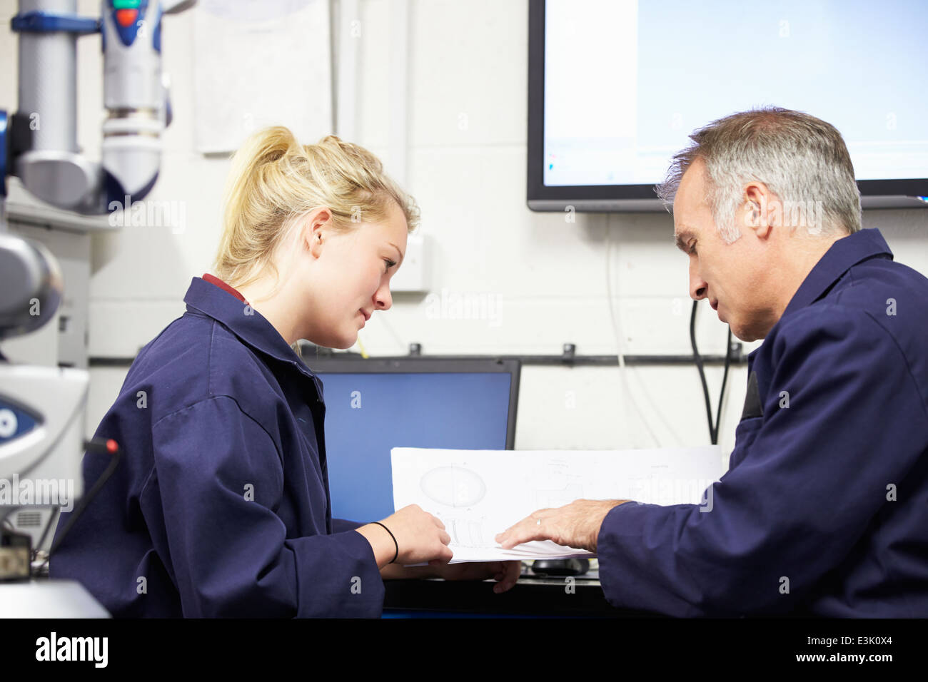 Engineer Showing Trainee Plans With CMM Arm In Foreground Stock Photo