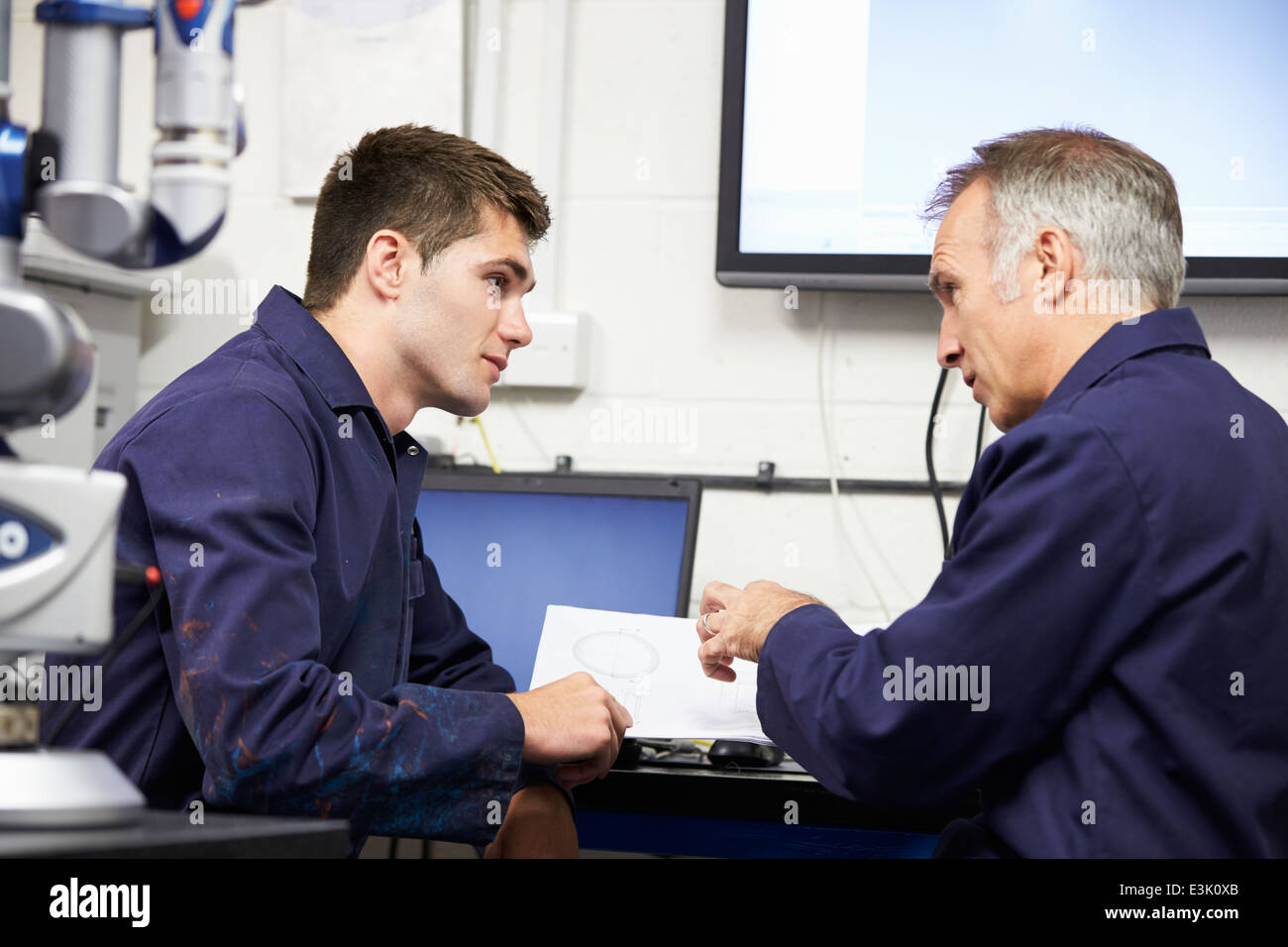 Engineer Showing Trainee Plans With CMM Arm In Foreground Stock Photo