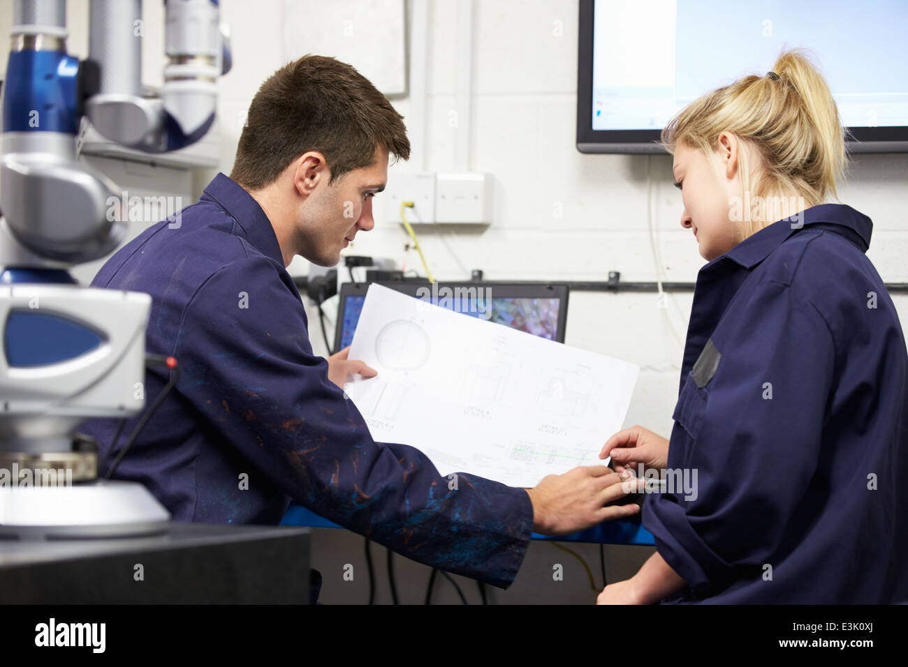 Trainee Engineers Studying Plans With CMM Arm In Foreground Stock Photo