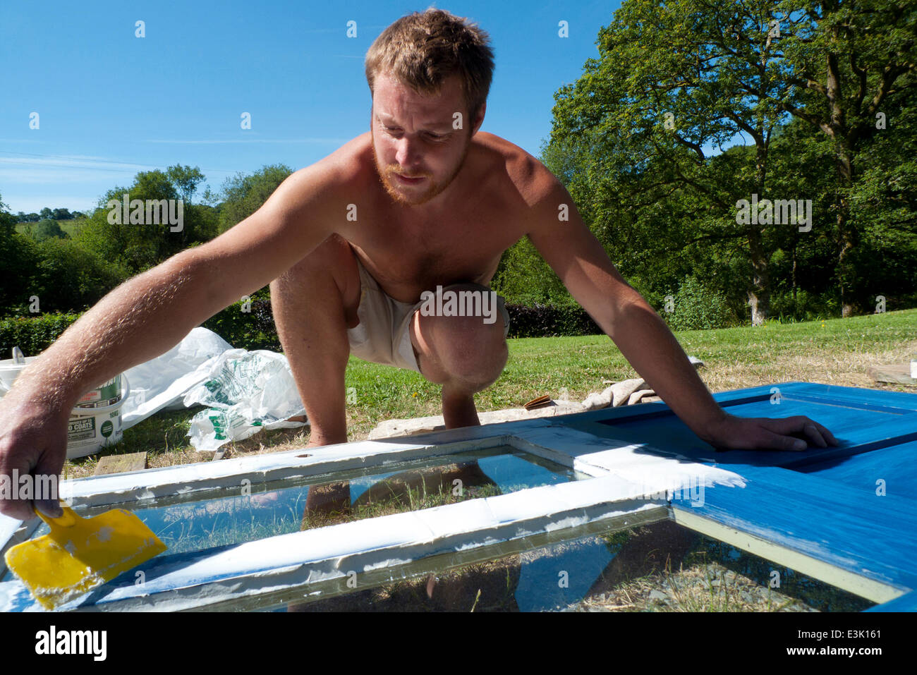 Llanwrda Carmarthenshire Wales UK, 24th June 2014.  Self-employed painter and decorator Ben Shipman takes advantage of fine weather and blue skies in rural West Wales to apply paint stripper to a client's door. The end of a settled period of two weeks of continuous sunshine is in view. Kathy deWitt/Alamy Live News Stock Photo