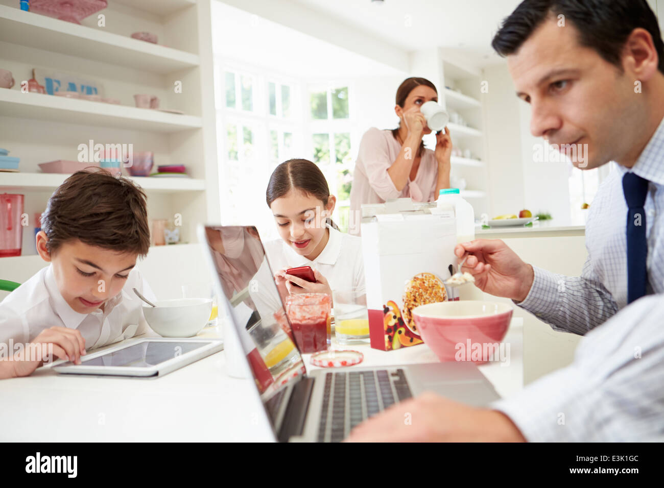 Family Using Digital Devices At Breakfast Table Stock Photo