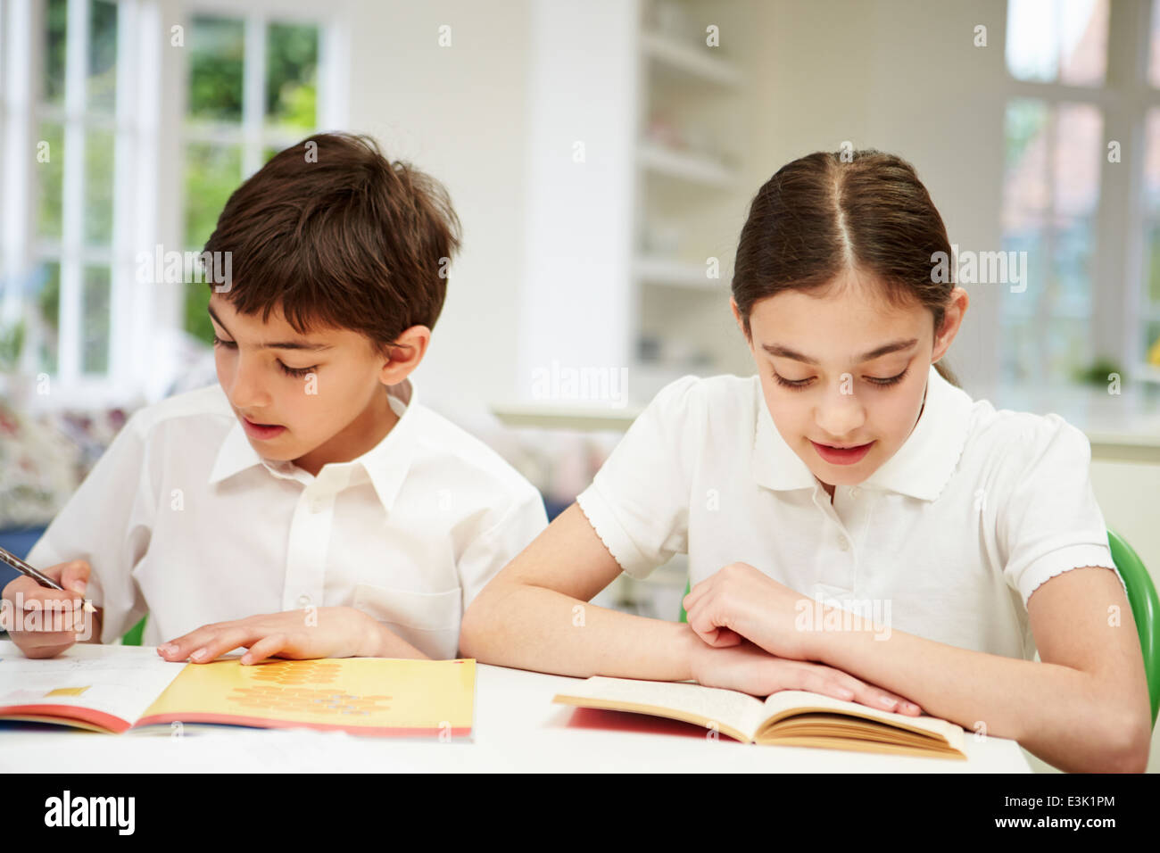 Children Wearing School Uniform Doing Homework In Kitchen Stock Photo