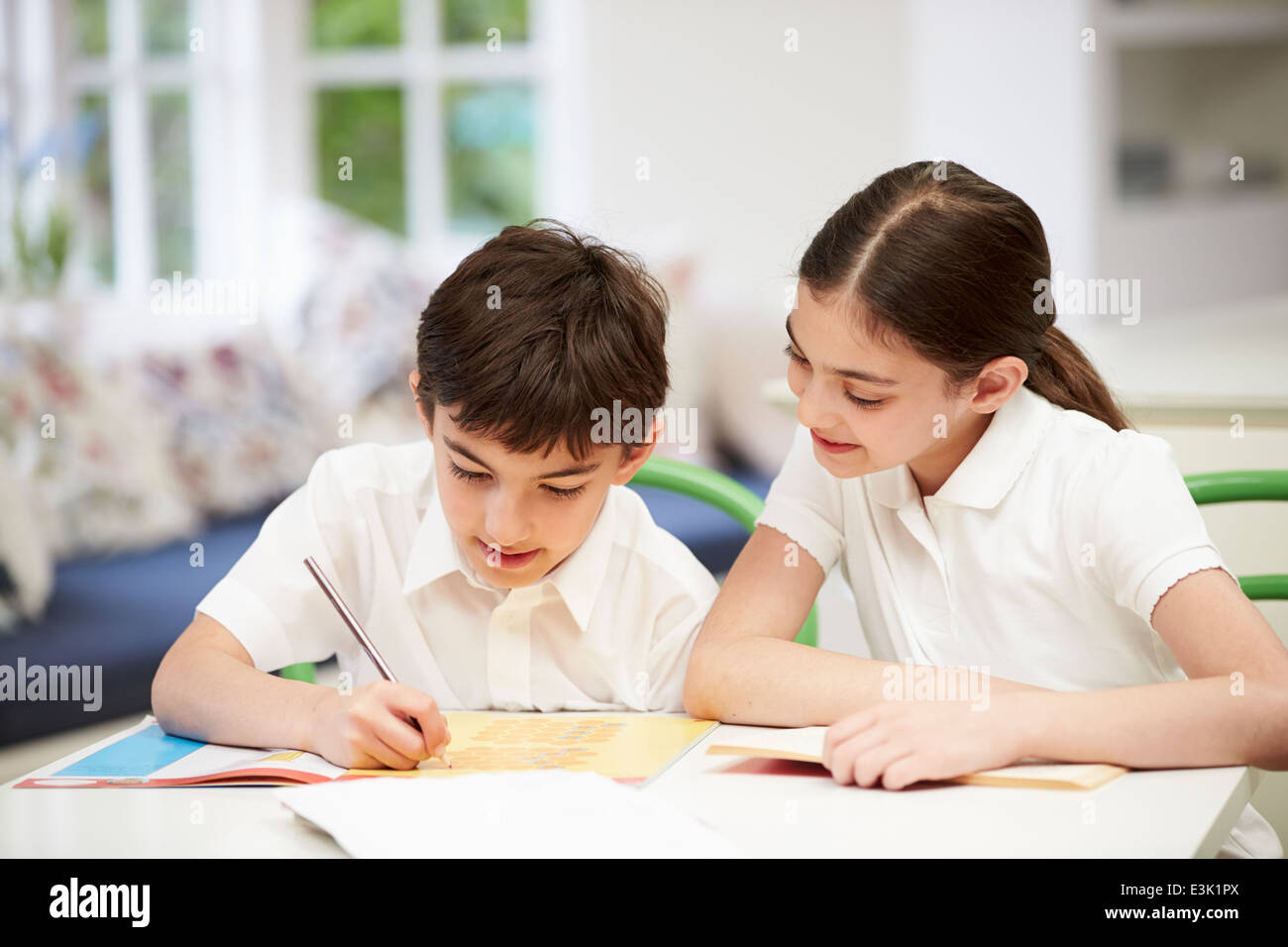 Children Wearing School Uniform Doing Homework In Kitchen Stock Photo