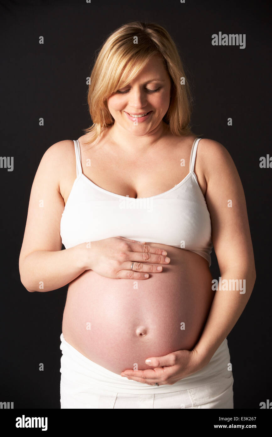 Portrait Of Pregnant Woman Wearing White On Black Background Stock Photo