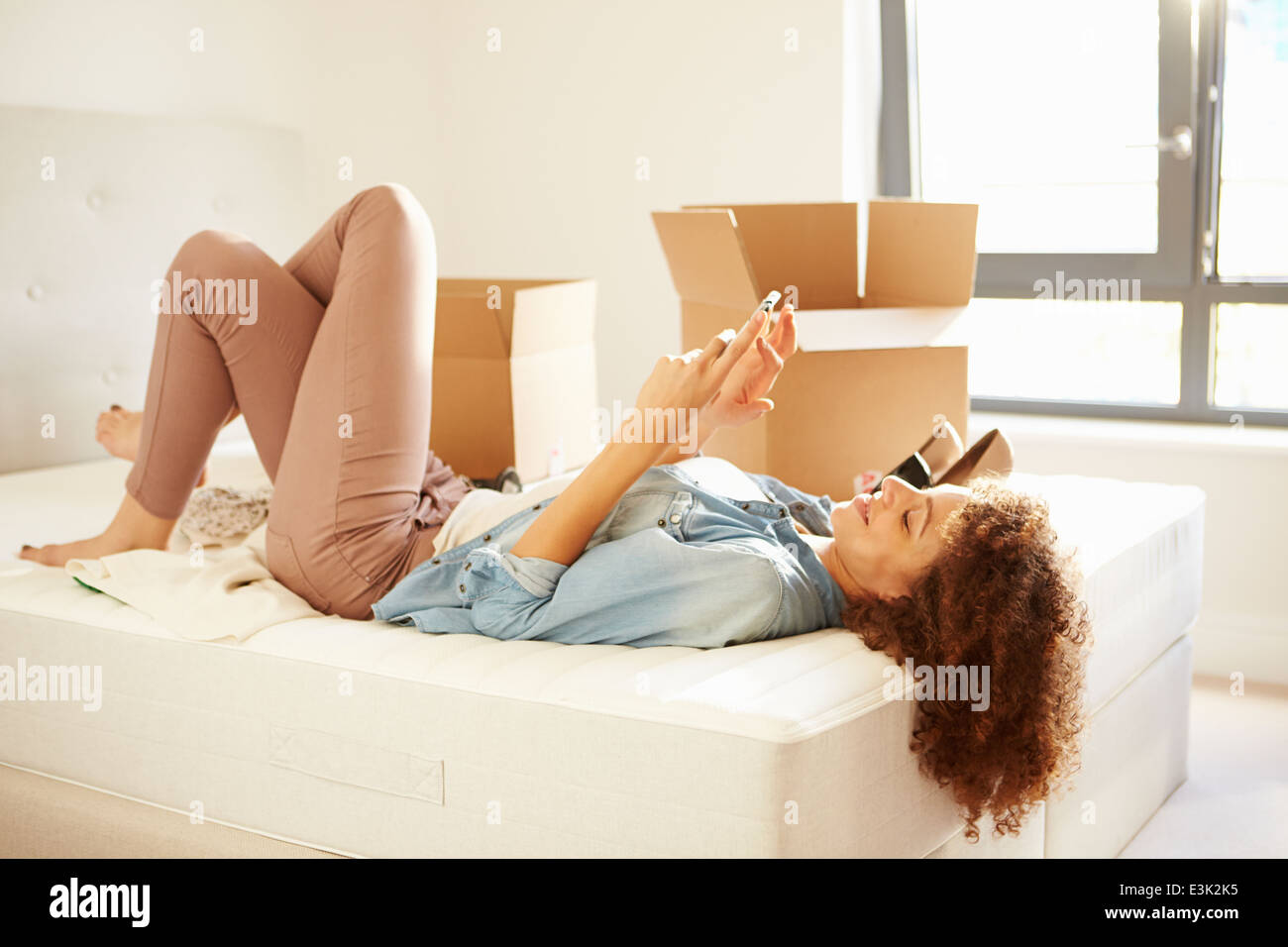 Woman Sending Text Message Having Moved Into New Home Stock Photo