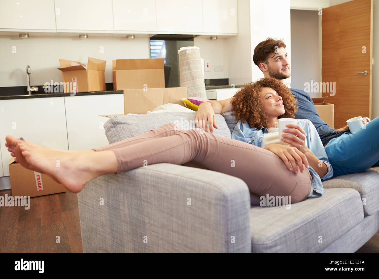 Couple Relaxing On Sofa With Hot Drink In New Home Stock Photo - Alamy