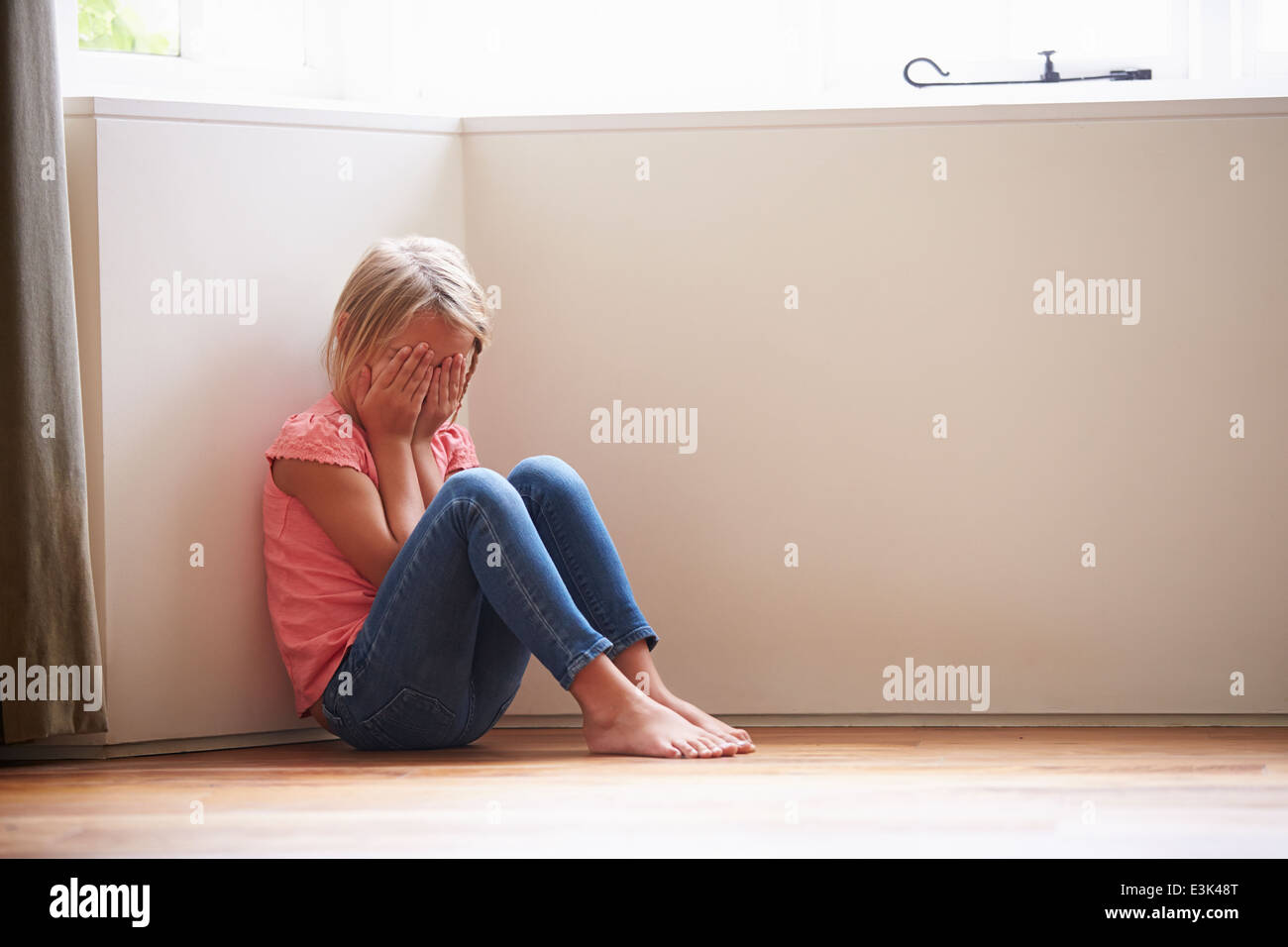 Unhappy Child Sitting On Floor In Corner At Home Stock Photo