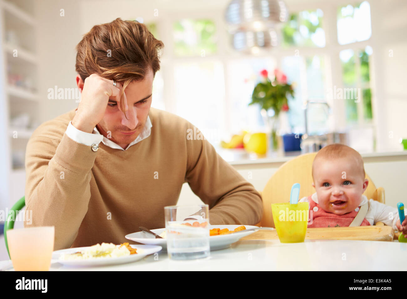 Father Feeling Depressed At Baby's Mealtime Stock Photo
