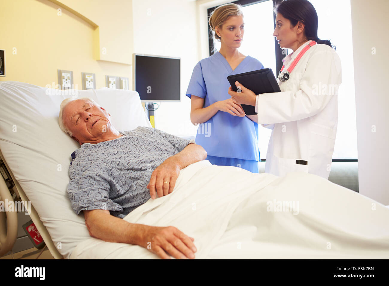 Medical Team Meeting As Senior Man Sleeps In Hospital Room Stock Photo