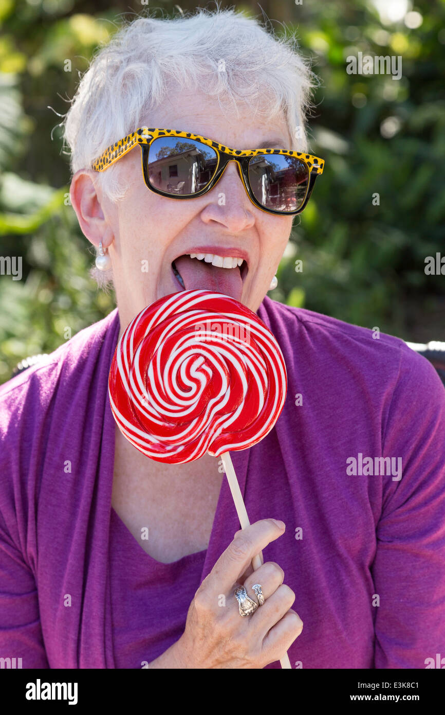 Happy Mature Woman in Sunglasses Enjoying Licking Her Oversized Lollipop, USA Stock Photo