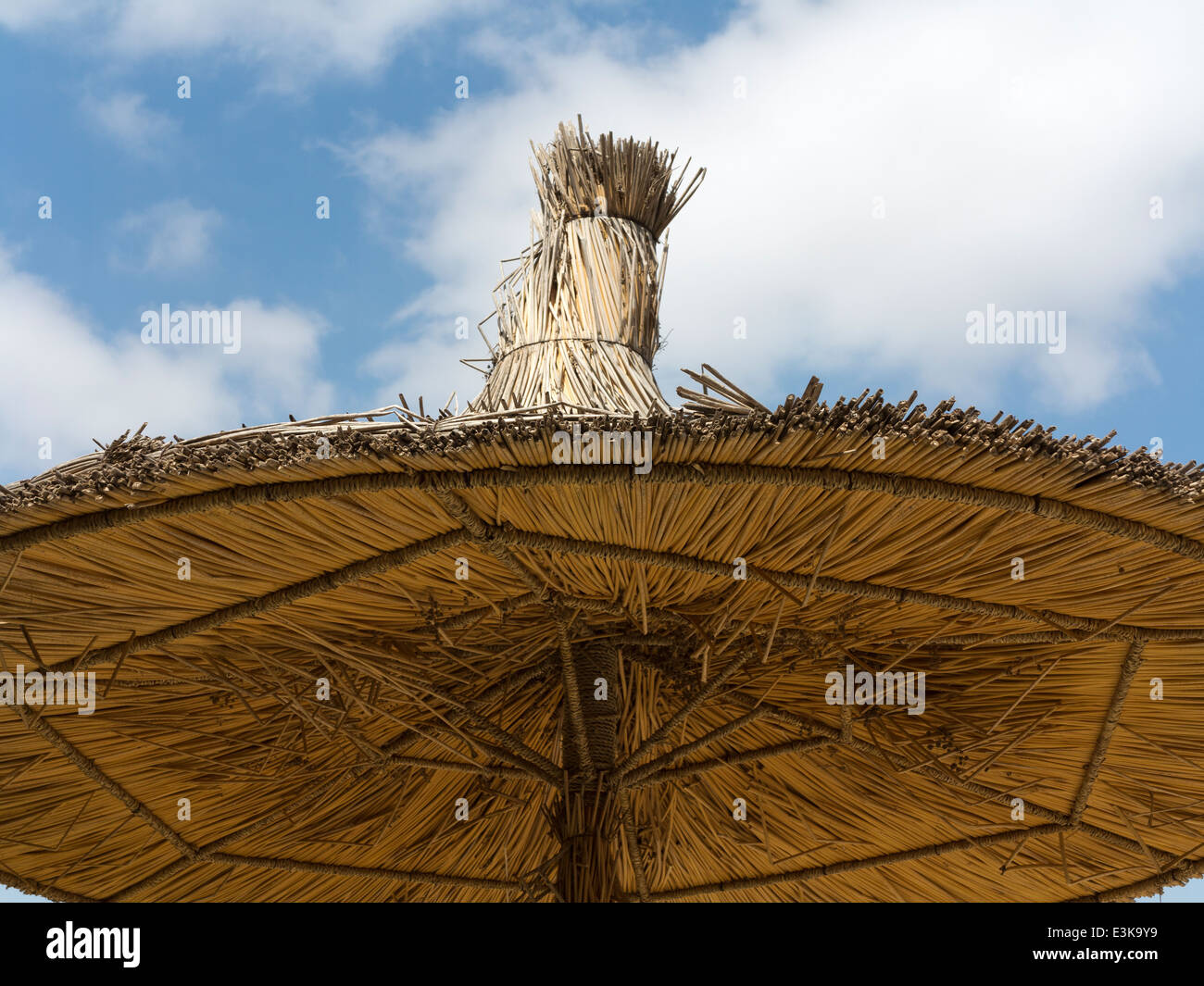 Detail of a section of straw sunshade umbrella looking up at the underside against a blue sky with light cloud Stock Photo