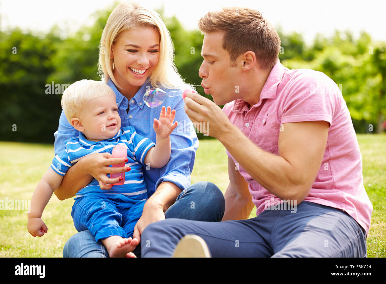 Parents Blowing Bubbles For Young Boy In Garden Stock Photo