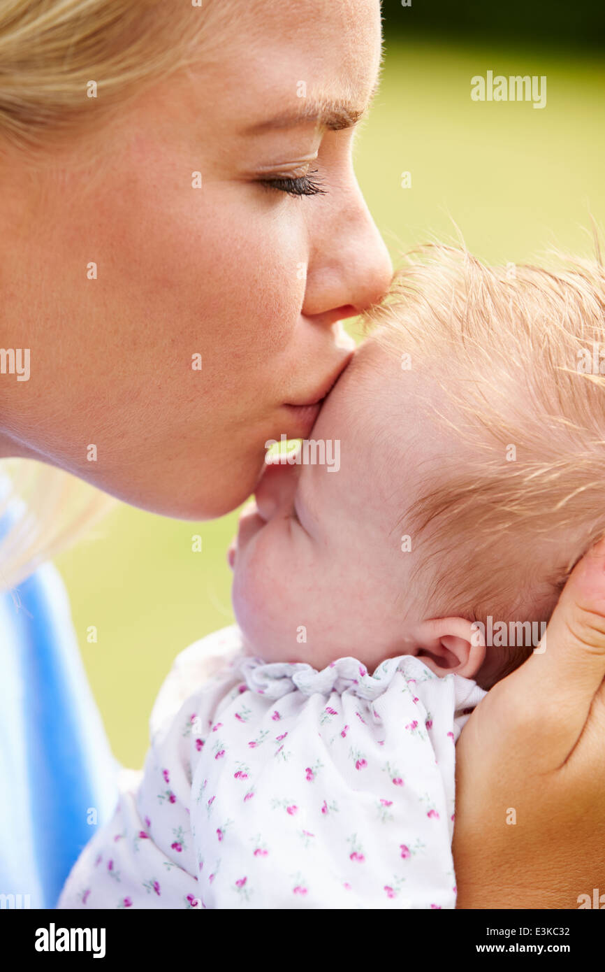 Loving Mother Kissing Baby Daughter In Garden Stock Photo