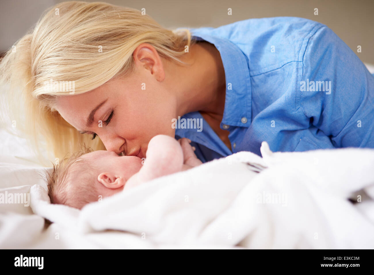 Mother Kissing Baby Girl As They Lie In Bed Together Stock Photo