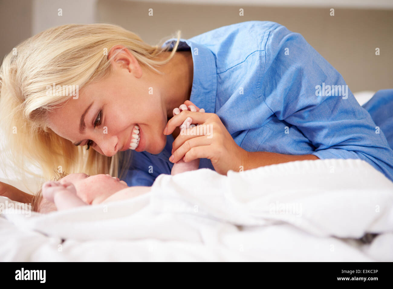 Mother Playing With Baby Girl As They Lie In Bed Together Stock Photo