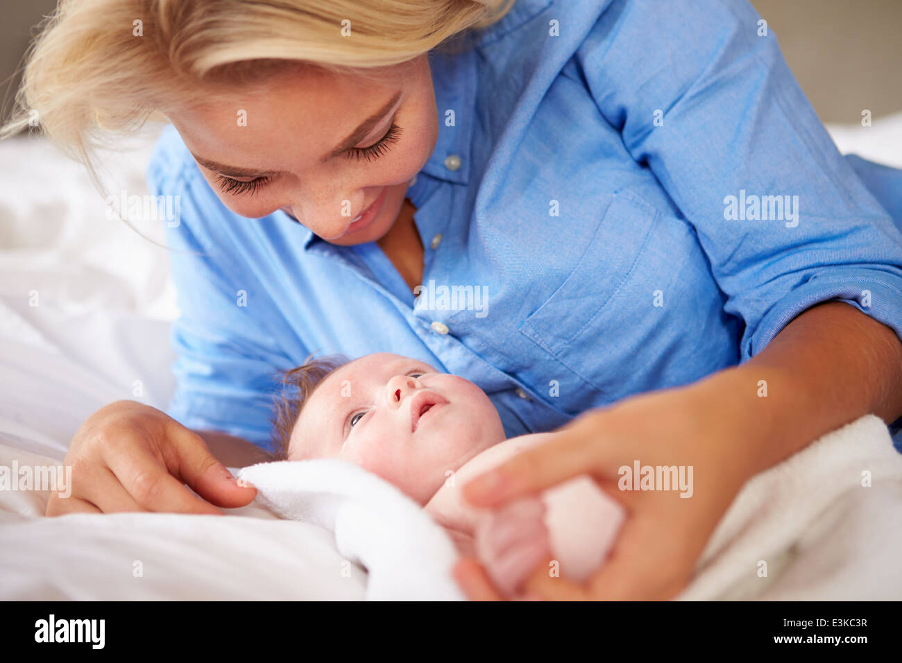 Mother Playing With Baby Girl As They Lie In Bed Together Stock Photo