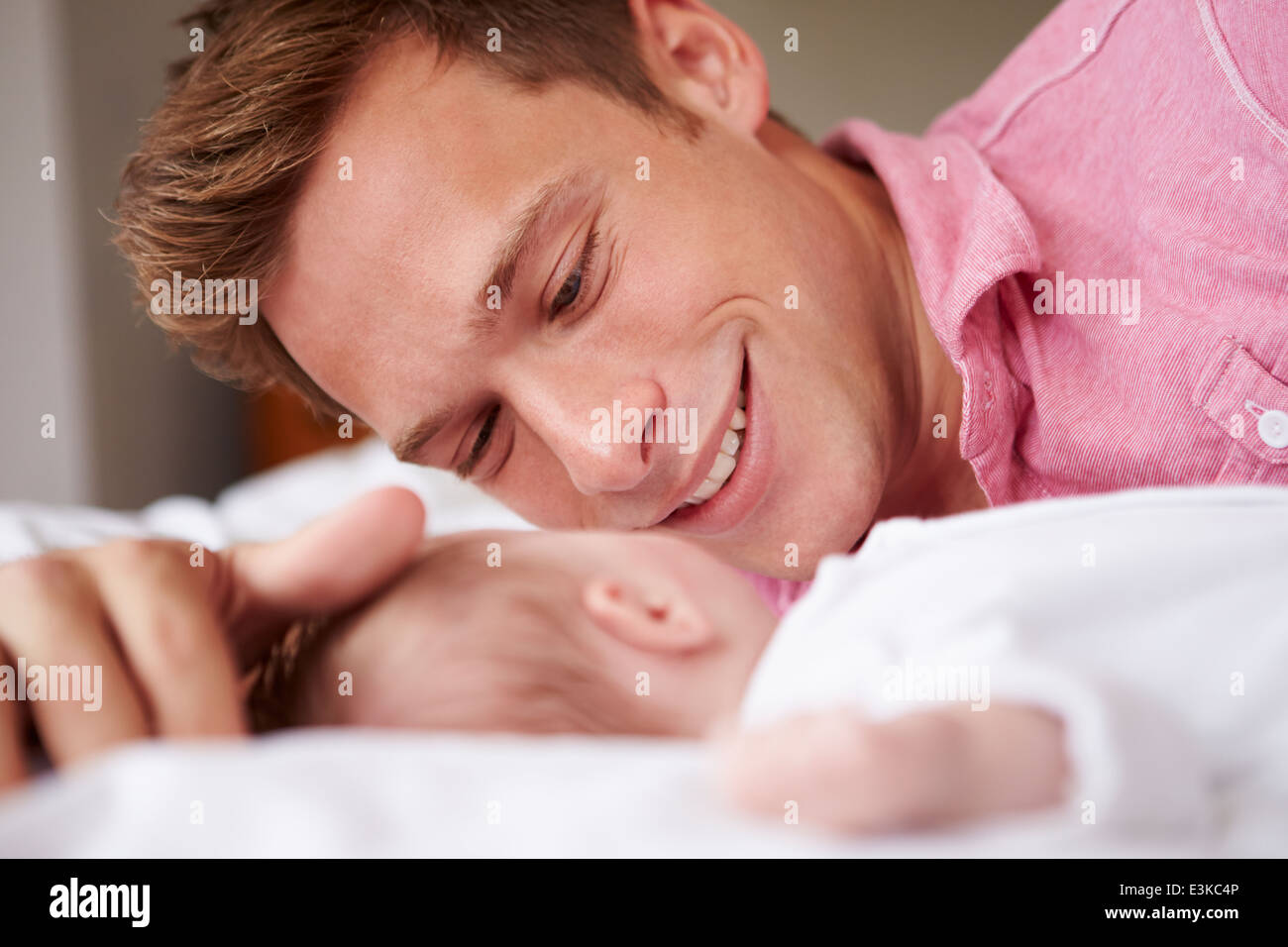 Father Playing With Baby Girl As They Lie In Bed Together Stock Photo