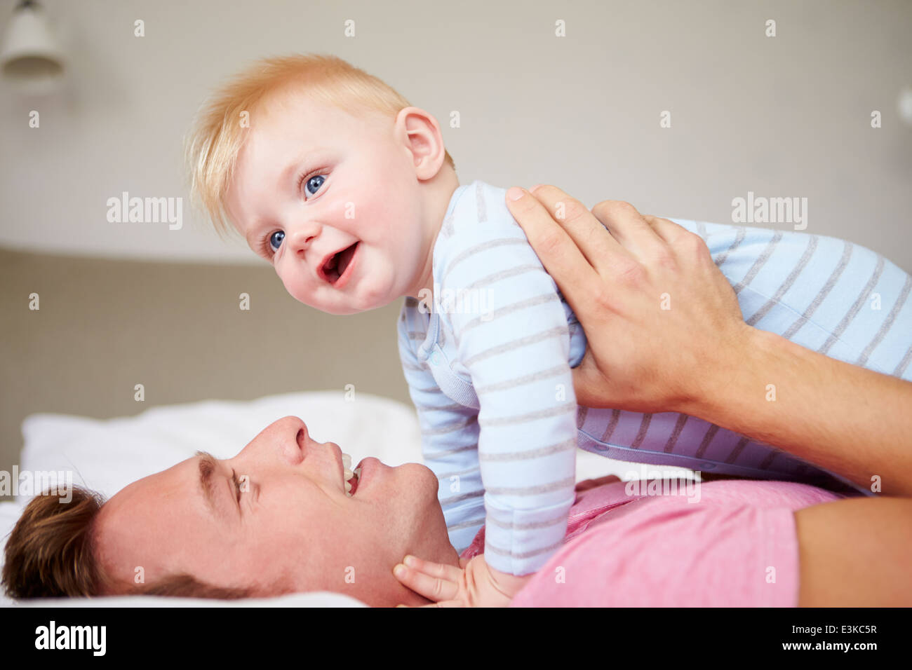 Father Playing With Baby Son As They Lie In Bed Together Stock Photo