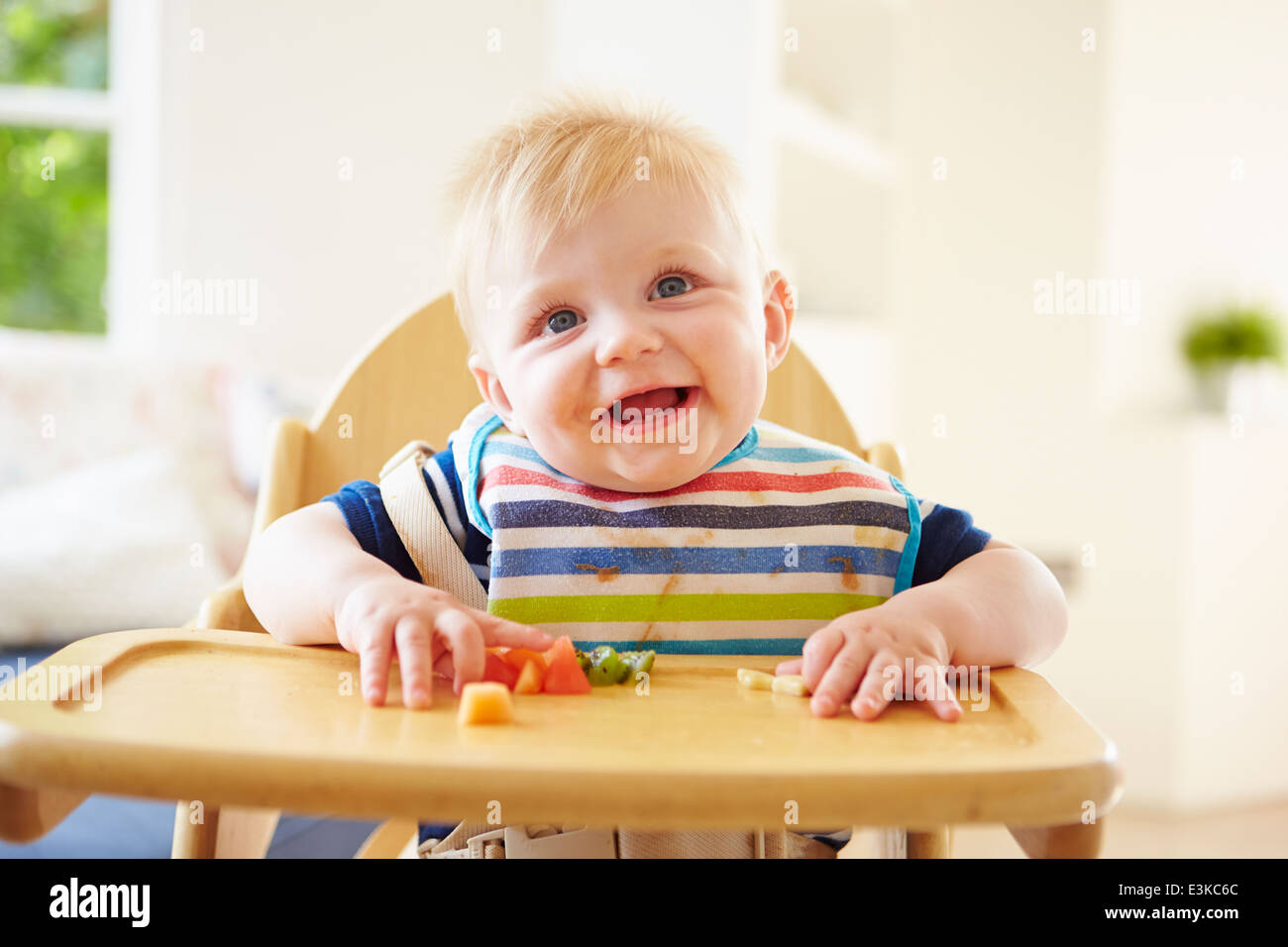 Baby Boy Eating Fruit In High Chair Stock Photo