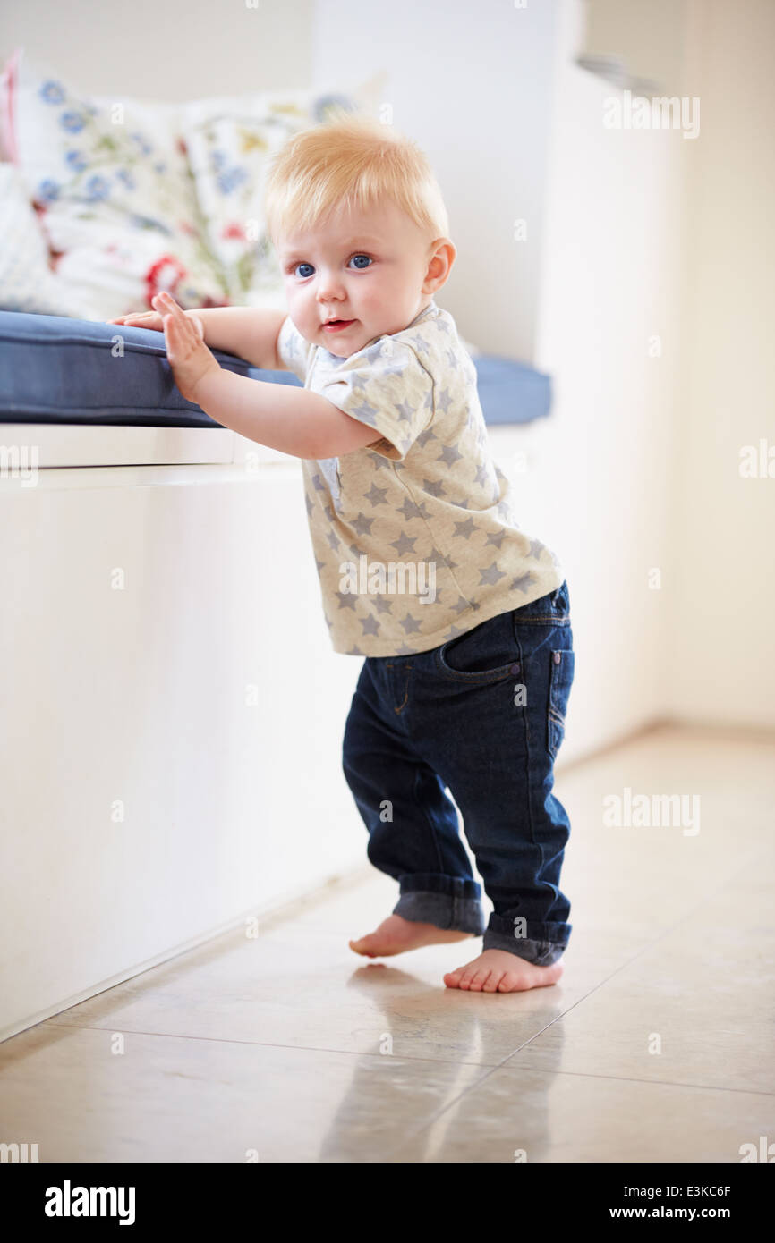 Young Boy Learning To Walk By Holding Onto Furniture Stock Photo