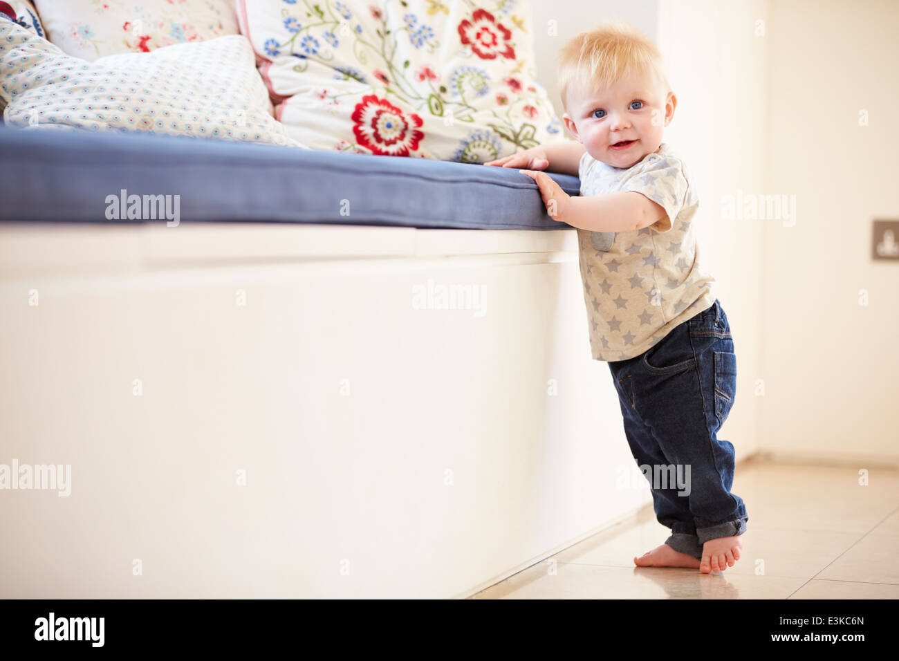 Young Boy Learning To Walk By Holding Onto Furniture Stock Photo