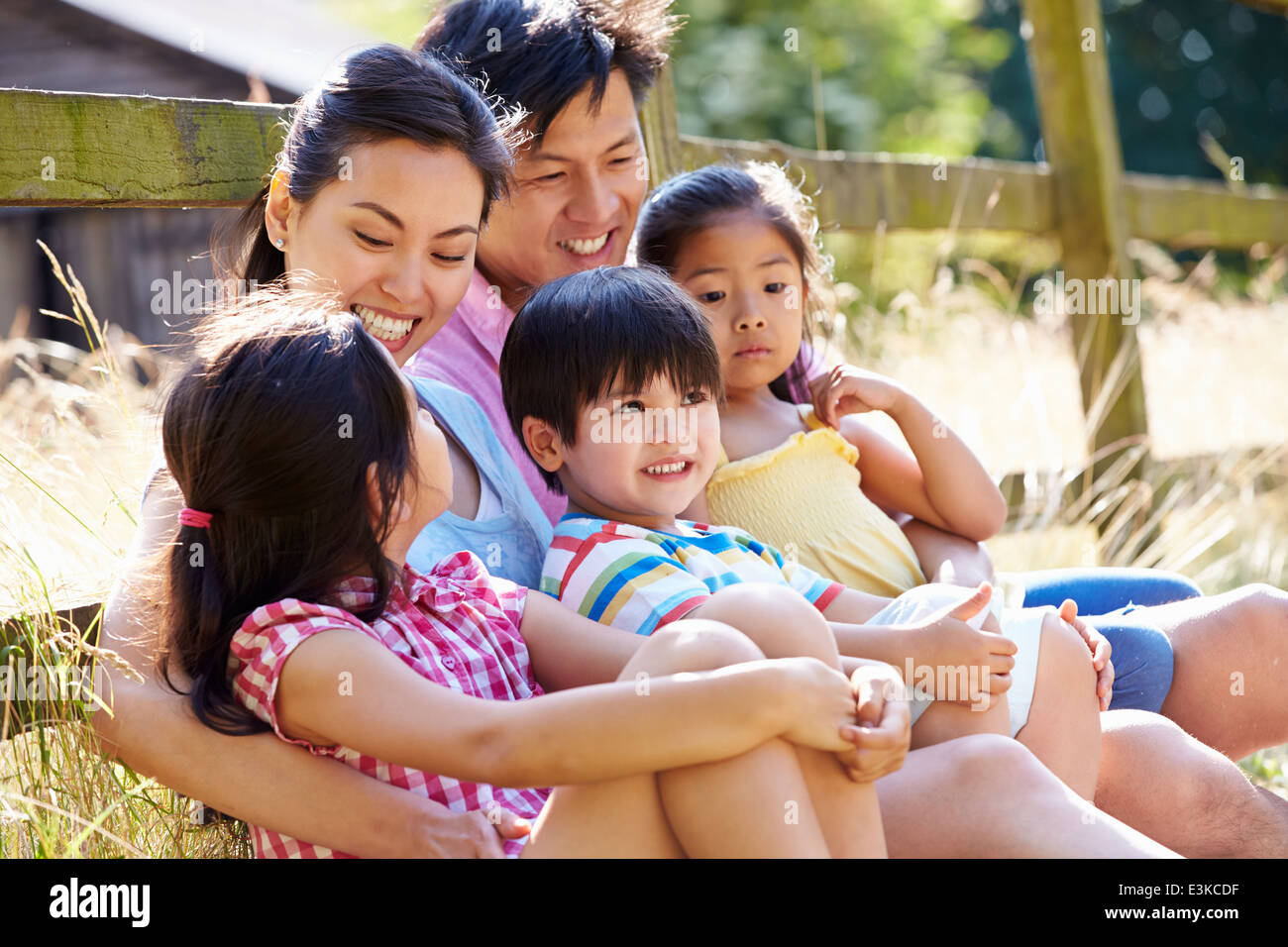 Asian Family Relaxing By Gate On Walk In Countryside Stock Photo