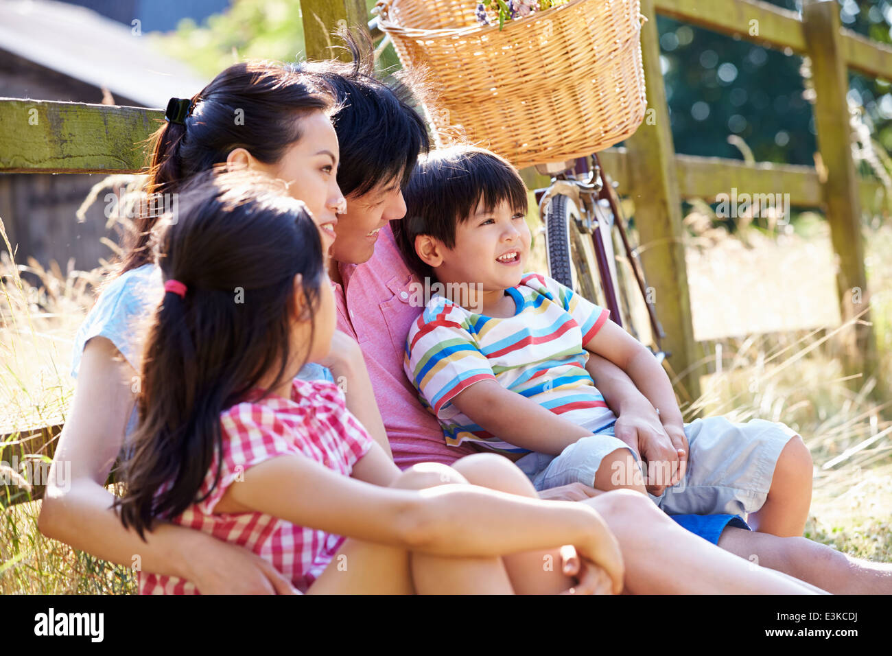 Asian Family Resting By Fence With Old Fashioned Cycle Stock Photo