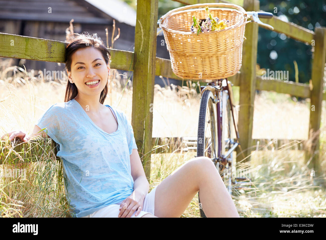 Asian Woman Resting By Fence With Old Fashioned Cycle Stock Photo