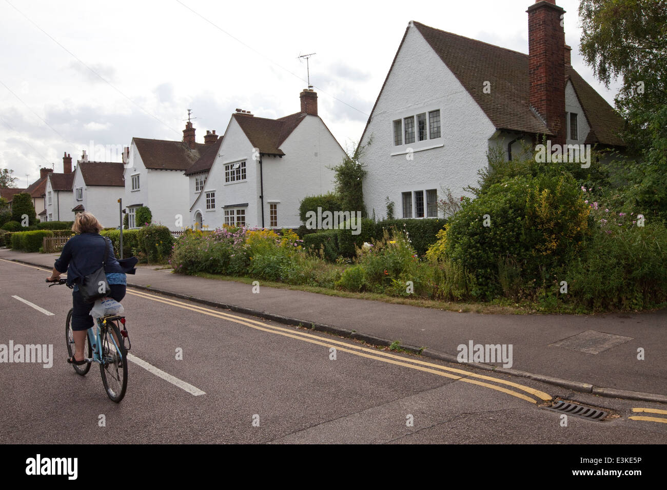 A woman cycles past Arts and Crafts period houses in Letchworth, the world's first Garden City, Letchworth, UK Stock Photo