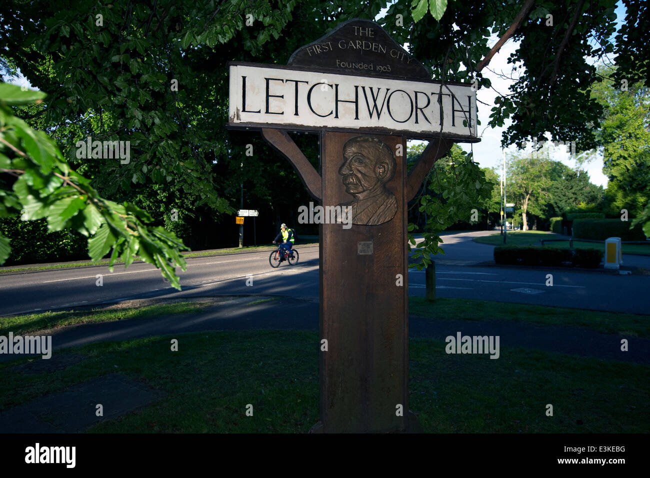 A cyclist rides past a road sign bearing the image of the founder of Letchworth Garden City, Ebenezer Howard. Letchworth. Stock Photo