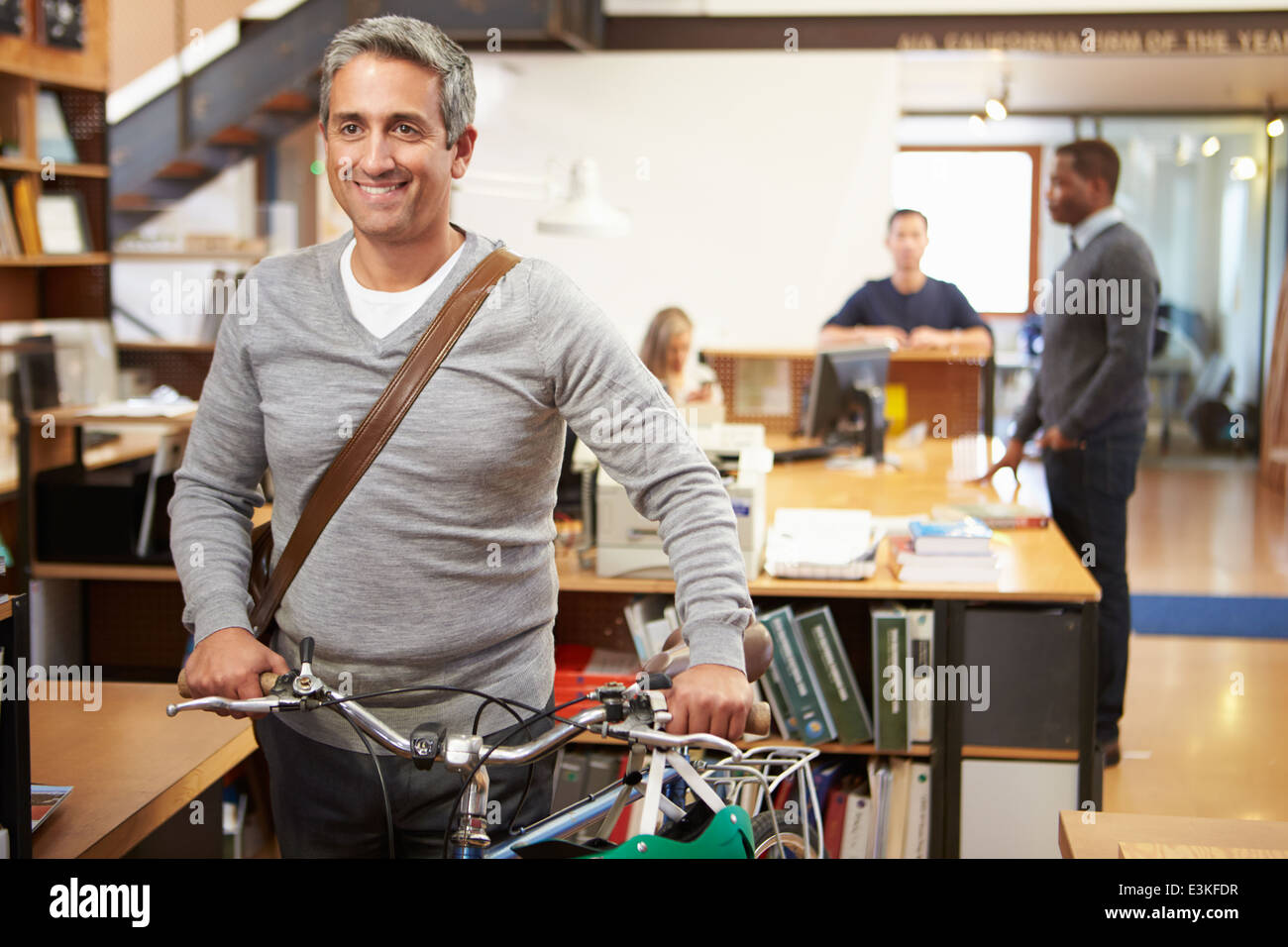 Architect Arrives At Work On Bike Pushing It Through Office Stock Photo