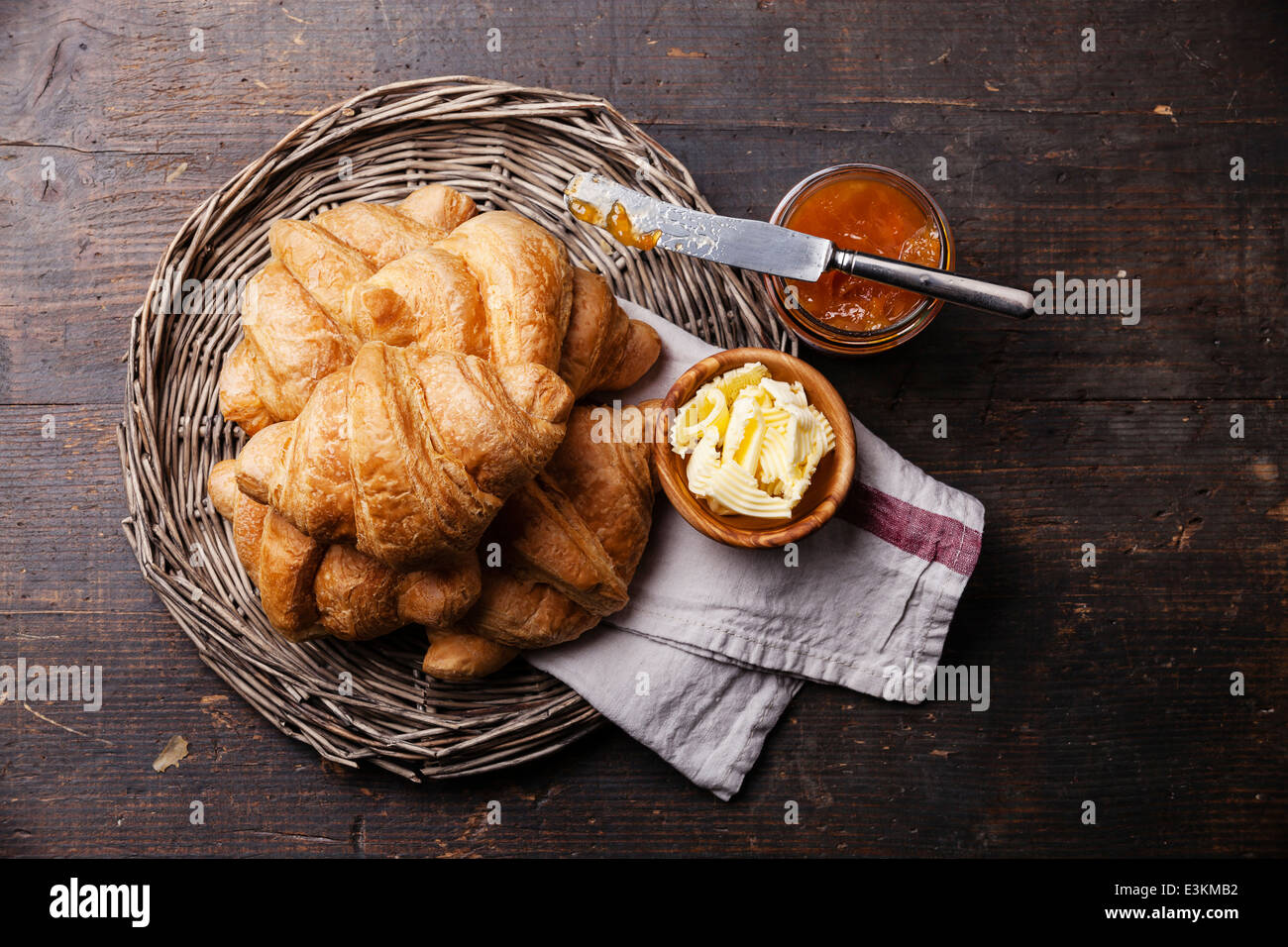 Croissants with butter and jam in wicker tray on dark wooden background Stock Photo