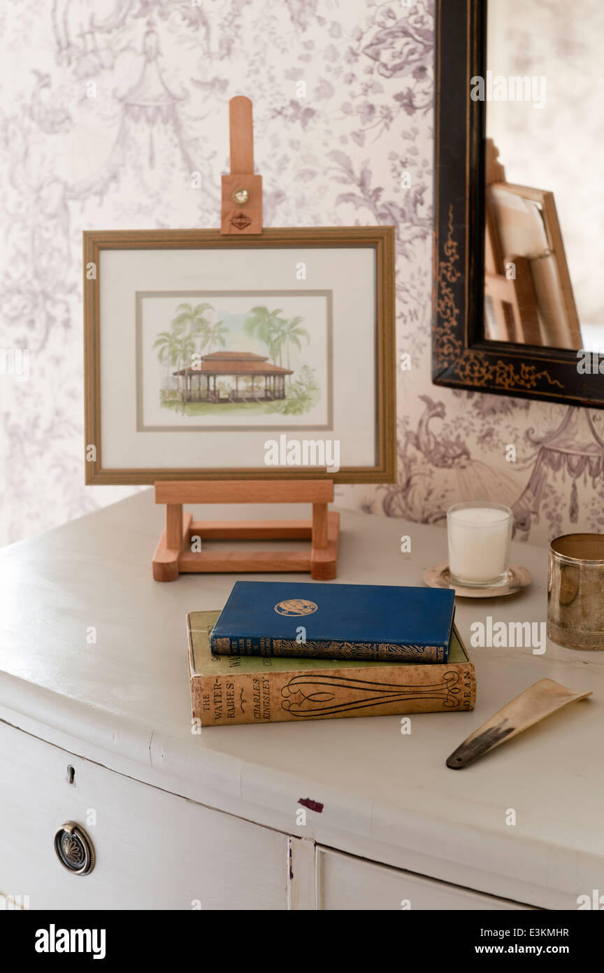 A Chinese watercolour on a miniatue easel on top of a chest of drawers along with a shoe horn and vintage books Stock Photo